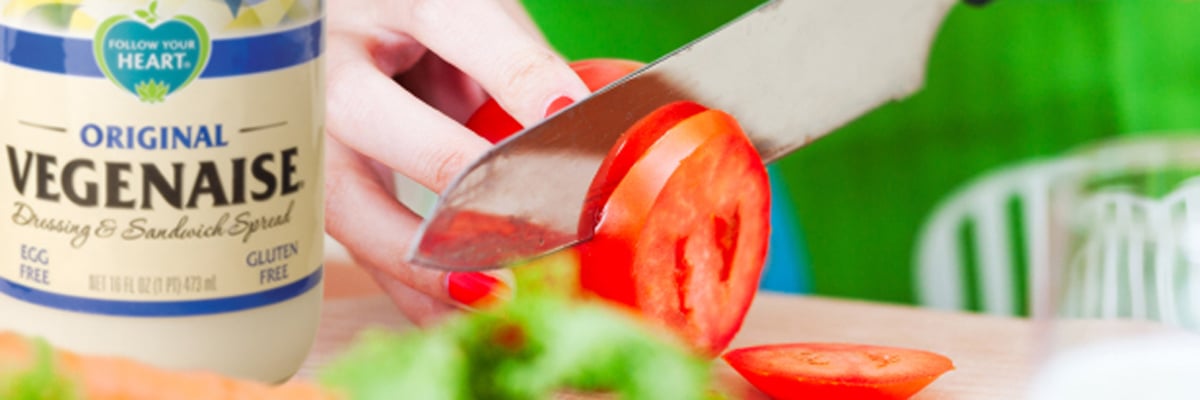 Person slicing a tomato next to a jar of Vegenaise